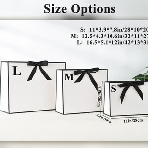 May include: Three white gift bags with black trim and black bows. Sizes are labeled S, M, and L, with dimensions in inches and centimeters. The smallest bag is 11 x 3.9 x 7.8 inches (28 x 10 x 20 cm).