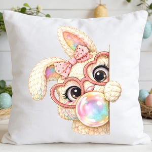 May include: White square pillow featuring a whimsical illustration of a bunny with heart-shaped glasses and a pink bow. The bunny is blowing a colorful bubble. Easter-themed decorative pillow.