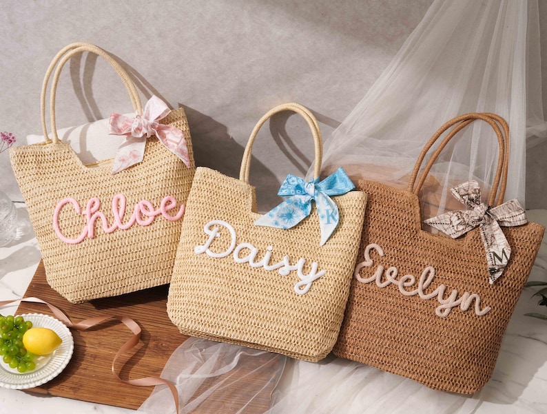 May include: Three woven straw tote bags with two top handles each. The bags feature personalized names in raised script lettering: Chloe in pink, Daisy in white, and Evelyn in white. Each bag is accented with a decorative fabric bow tied to one handle.