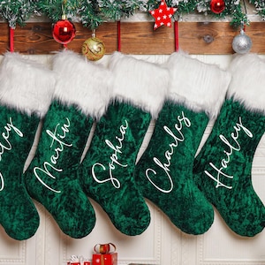 Puede incluir: Cinco calcetines navideños verdes con ribete de piel sintética blanca cuelgan de un estante de madera. Cada calcetín está personalizado con un nombre en escritura blanca: Bailey, Martin, Sophia, Charles y Hailey. Decoración festiva.