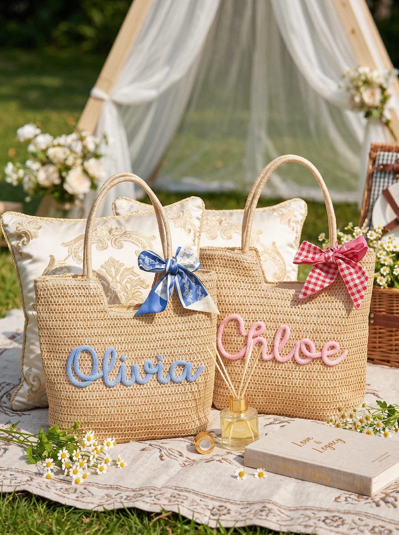 May include: Two woven straw tote bags with top handles. One bag features the name Olivia in blue script with a blue patterned ribbon. The other bag features the name Chloe in pink script with a red and white checkered ribbon tied to the handle.