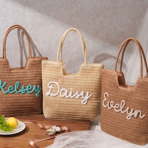 May include: Three woven straw tote bags with two top handles each. The left bag is dark brown with the name Kelsey in teal script. The center bag is light beige with the name Daisy in white script. The right bag is brown with the name Evelyn in white.