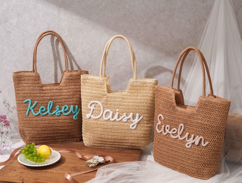 May include: Three woven straw tote bags with two top handles each. The left bag is dark brown with the name Kelsey in teal script. The center bag is light beige with the name Daisy in white script. The right bag is brown with the name Evelyn in white.