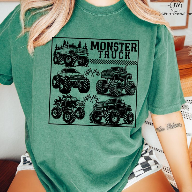 May include: A teal green t-shirt featuring a black graphic of six monster trucks with large tires. The text "MONSTER TRUCK" is printed above the trucks in a black, bold font. Checkered flags are also included in the design.