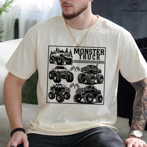 May include: Cream-colored t-shirt featuring a black and white graphic of six monster trucks. The text "MONSTER TRUCK" is displayed above the trucks. The design includes checkered flags and a forest silhouette.