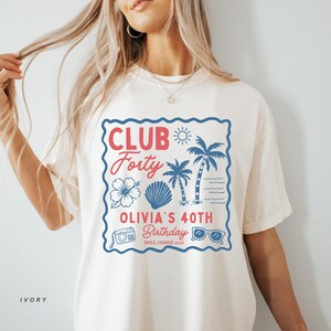 May include: An ivory t-shirt featuring a blue scalloped square frame containing red and blue graphics. Text reads CLUB Forty, OLIVIA'S 40TH Birthday, and MAUI, HAWAII 2026. Graphics include a sun, palm trees, a hibiscus flower, a seashell, a camera, and sunglasses.
