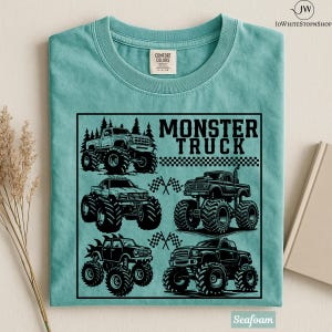 May include: Seafoam green t-shirt featuring a black graphic of several monster trucks. The graphic includes the words "MONSTER TRUCK" and checkered flags. The shirt is made of a soft material.