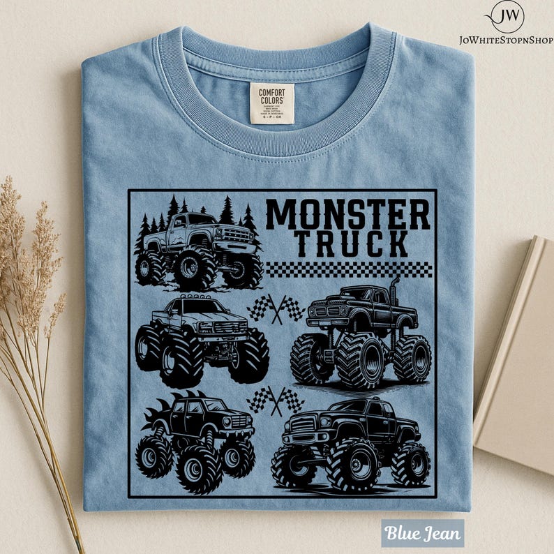 May include: Blue jean t-shirt featuring a black graphic of several monster trucks with large tires. The words "MONSTER TRUCK" are printed in bold, black letters above the trucks. The shirt has a classic crew neck and short sleeves.