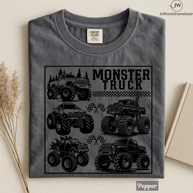 May include: A gray Comfort Colors t-shirt featuring a black graphic of several monster trucks. The text "MONSTER TRUCK" is displayed above the trucks. The shirt is folded and has a tag at the top.