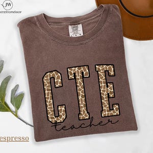 May include: Espresso-colored t-shirt with the letters "CTE" in a giraffe print design, outlined in black. The word "teacher" is written in a cursive font below the letters. The shirt is a Comfort Colors brand.