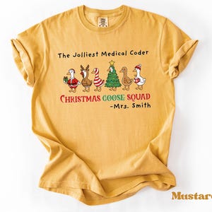 May include: Mustard-coloured t-shirt with the text "The Jolliest Medical Coder" and "Christmas Goose Squad." The shirt features a graphic of geese dressed in Christmas attire. The name "Mrs. Smith" is also printed on the shirt.