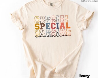 Pode incluir: Camiseta cor marfim com as palavras "SPECIAL EDUCATION" em um design retrô empilhado. A palavra "SPECIAL" está em letras coloridas em negrito, enquanto "EDUCATION" está em itálico. A camiseta tem mangas enroladas.