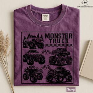 May include: Berry-colored t-shirt featuring a black graphic of several monster trucks. The text "MONSTER TRUCK" is displayed above the trucks. The shirt has a crew neck and short sleeves. The Comfort Colors tag is visible.
