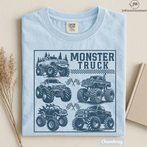 May include: Light blue t-shirt with a graphic of several monster trucks in a square frame. The words "MONSTER TRUCK" are printed in a bold font above the trucks. The shirt is made of a soft, comfortable material.