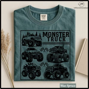 May include: Blue spruce t-shirt featuring a black graphic of four monster trucks with large tires and checkered flags. The words "MONSTER TRUCK" are printed in bold, black letters above the trucks. The shirt has a crew neck and a Comfort Colors tag.