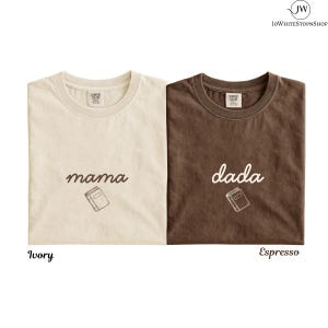 May include: Two short-sleeve crew neck t-shirts. The left shirt is ivory with the word mama and a small book graphic in brown. The right shirt is espresso brown with the word dada and a small book graphic in white. Both have Comfort Colors labels.