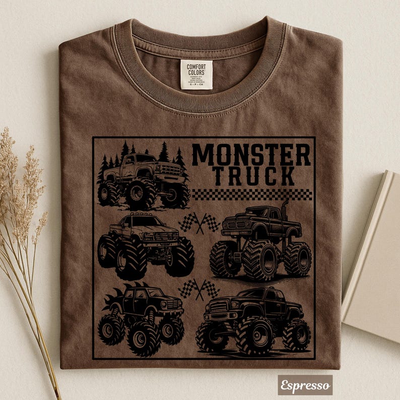 May include: Espresso-colored t-shirt featuring a black graphic of four monster trucks with large tires. The text "MONSTER TRUCK" is above a checkered flag design. The shirt is made of Comfort Colors material.