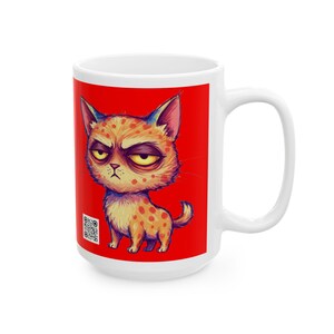 以下が含まれることがあります： 赤い背景に、オレンジと黄色の斑点のある不機嫌そうな猫の漫画が描かれた白いセラミックマグカップ。猫は眉をひそめ、黄色い目をした不機嫌そうな表情をしている。