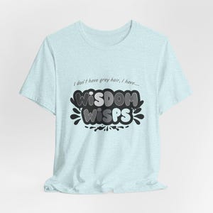 May include: Light blue t-shirt with the text "I don't have grey hair, I have... WISDOM WISPS" in a black and grey design. The shirt has short sleeves and a crew neck.