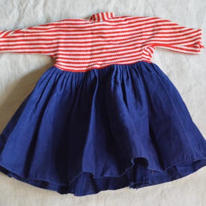Peut inclure: Une robe de poupée vintage avec un haut en tricot rayé rouge et blanc et une jupe bleu marine. La robe a des manches courtes et un col montant. Le tissu semble être du coton ou une matière similaire.