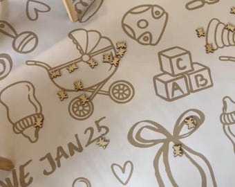 May include: A white canvas with brown outlines of baby-related items, such as a baby carriage, a rattle, a pacifier, and a bow. The canvas has the text "Due Jan 25" written on it. There are wooden cutouts of bears scattered on the canvas.