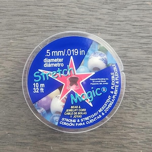 May include: A spool of clear stretch magic bead and jewellery cord. The spool is labelled with the text "Stretch Magic" and "Bead & Jewellery Cord/Cable de Cuentas y Joyas". The spool is 10 metres or 32 feet long and the cord is 0.5 mm or 0.019 inches in diameter.