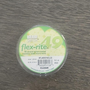 May include: A spool of clear Bead Smith flex-rite 49 strand nylon-coated stainless steel micro-wire. The spool is labelled with the brand name, product name, size, and break strength. The spool is 30 m (98 ft) long and has a break strength of 182 lb.