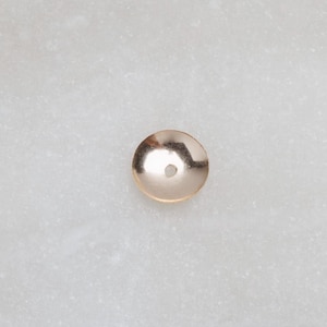 Puede incluir: Una pequeña cuenta redonda de metal de color dorado con un agujero en el centro.