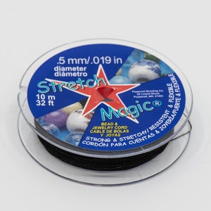 Puede incluir: Un carrete de cordón elástico mágico negro para cuentas y joyas. La etiqueta dice "Stretch Magic" con el texto "Bead & Jewelry Cord/Cable de Bolás Joyas" y "Strong & Stretchy/Resistente & Flexible" en inglés y español. La etiqueta también indica que el cordón tiene 10 metros o 32 pies de largo y un diámetro de 0,5 mm o 0,019 pulgadas.