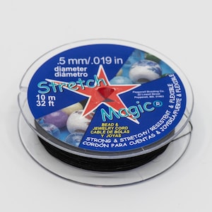 May include: A spool of black stretch magic bead and jewellery cord. The label reads "Stretch Magic" with the text "Bead & Jewellery Cord, Cable de Bolás, Joyas, Strong & Streton/Resistent & Flexible, Cordon para Cuentas & Joyeria Fuerte & Flexible". The label also states "5 mm/.019 in diameter, diametro, 10 m, 32 ft".