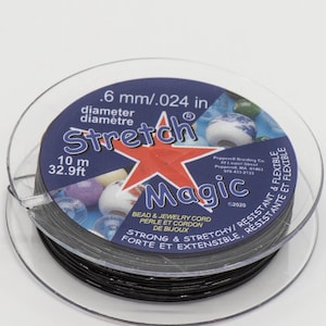 May include: A spool of black stretch magic bead and jewellery cord. The spool is labelled with the text .6 mm/.024 in diameter, 10 m, 32.9ft, and Stretch Magic. The label also says Bead & Jewellery Cord, Perle et Cordon de Bijoux, Strong & Stretchy/Resistante et Flexible, Forte et Extensible/Resistante et Flexible.