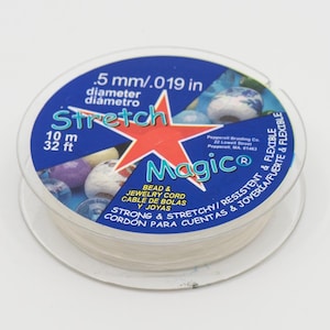 May include: A spool of white stretch magic bead and jewellery cord. The spool is labelled with the text "Stretch Magic", "Bead & Jewellery Cord", "Cable de Bolás y Joyas", "Strong & Stretchy/Resistent & Flexible", "Cordon para Cuentas & Joyas", "10 m", "32 ft", ".5 mm/.019 in", and "diameter/diametro".
