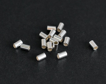 May include: A group of silver-colored metal crimp beads scattered on a black surface.