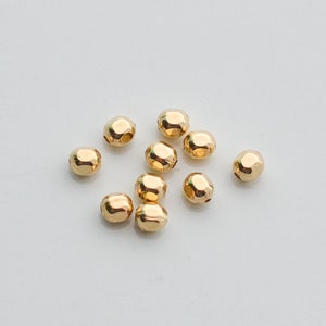 May include: A collection of small, gold-colored beads with a faceted surface. The beads are scattered on a white background. These beads are suitable for jewelry making and crafting projects.