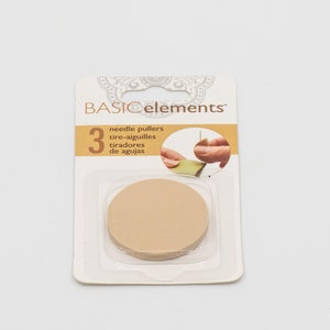 May include: A package of three beige needle pullers from Basic Elements. The package includes a clear plastic tray with three round, beige needle pullers. The packaging also features the text "needle pullers" in English, French, and Spanish.