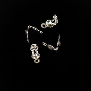 May include: Four silver metal clasps for jewelry making. The clasps are in the shape of a loop with a small ball on the end.