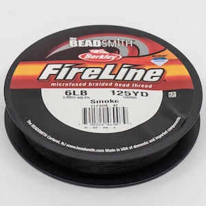 May include: A spool of black FireLine microfused braided bead thread by Berkley. The spool is labeled with the text "6LB 125YD Smoke".