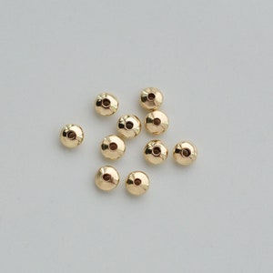 May include: A group of 10 gold-colored metal beads, each with a small hole in the center. The beads are arranged in a loose cluster on a white surface.