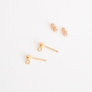 May include: Two pairs of gold earring backs. One pair is a traditional post back, and the other pair is a ball post back.