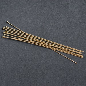 May include: A bundle of gold-colored head pins, also known as straight pins, are arranged in a fan shape on a black surface.
