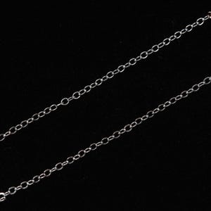May include: A silver chain necklace with a delicate, linked design. The chain is shown against a black background.
