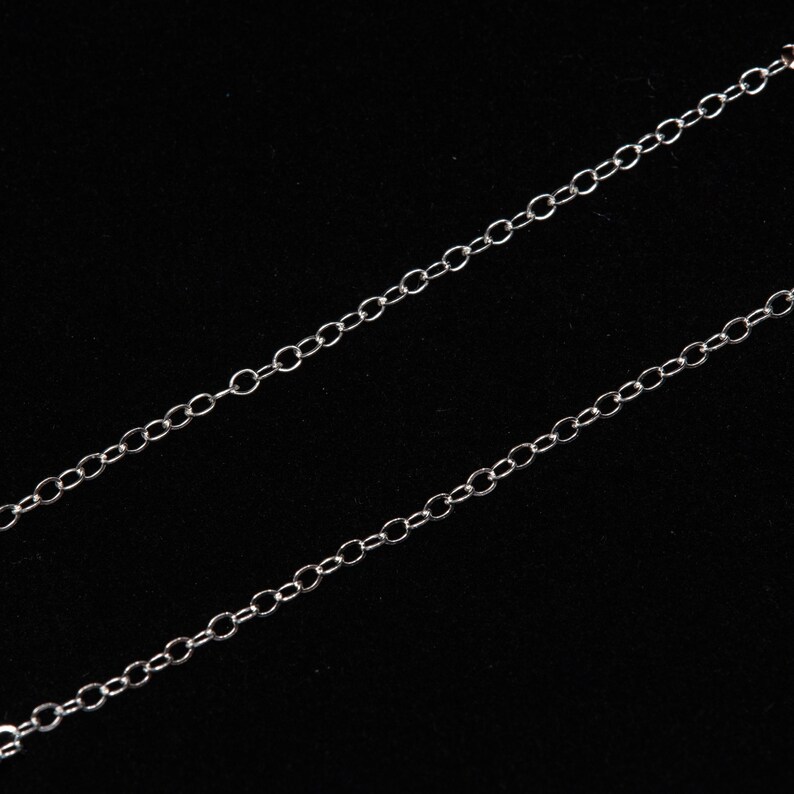 May include: A silver chain necklace with a delicate, linked design. The chain is shown against a black background.