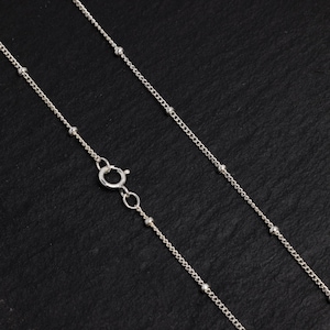 May include: A silver chain necklace with small round beads. The chain is delicate and has a simple design.