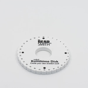 Puede incluir: Disco Kumihimo de plástico blanco con texto y números negros. El texto dice "mini Kumihimo Disk Create your own braided cord!" y "the BEAD SMITH®".