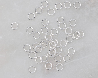 May include: A pile of silver jump rings, a type of jewelry finding used for connecting chains, cords, and other jewelry components.