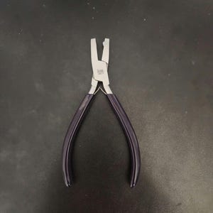 K&ouml;nnte beinhalten: Eine Zange aus silberfarbenem Metall mit violetten Griffen. Die Zange hat einen kleinen, flachen Kiefer und ist zum Biegen und Formen von Schmuck gedacht.