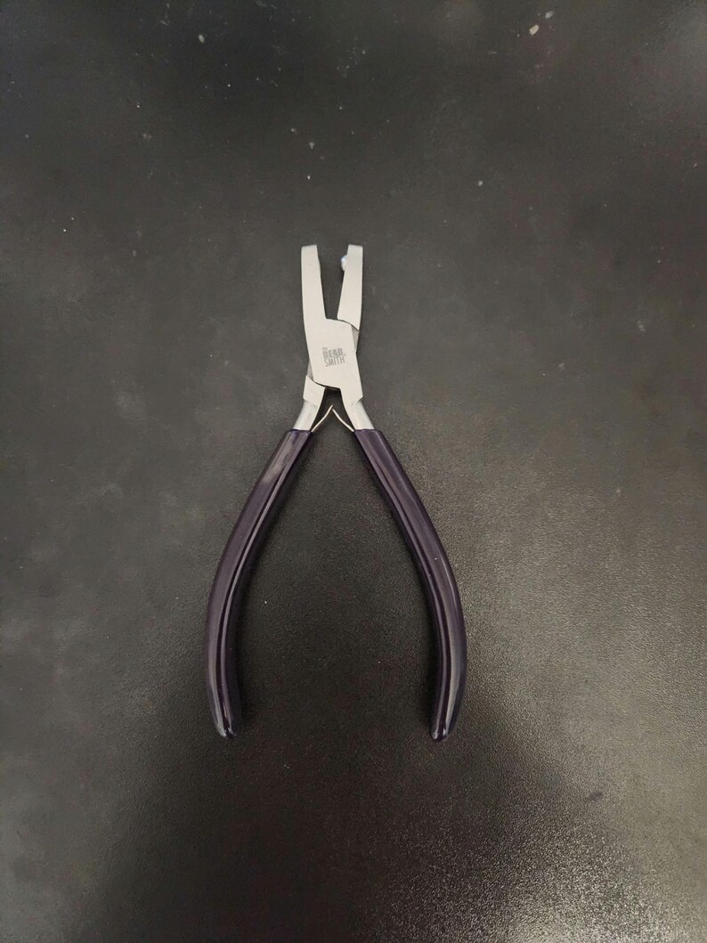 K&ouml;nnte beinhalten: Eine Zange aus silberfarbenem Metall mit violetten Griffen. Die Zange hat einen kleinen, flachen Kiefer und ist zum Biegen und Formen von Schmuck gedacht.