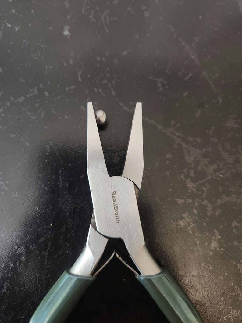 May include: Close-up of a pair of silver beading pliers with green handles. The pliers are open and the text "BeadSmith" is visible on the metal.