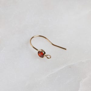 May include: Gold earring with a red gemstone. The earring has a hook closure.