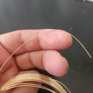 May include: A close-up of a spool of gold-colored wire. The wire is thin and appears to be made of metal.